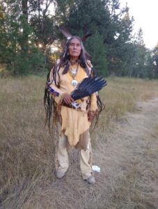 Thomas White Eagle standing by a path in Native AMerica authentic clothing