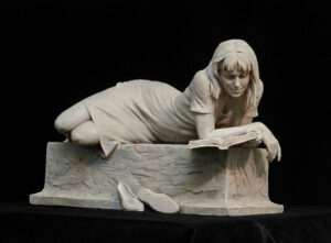 Bronze sculpture by Blair Buswell of a young woman laying on a pedestal, reading a book
